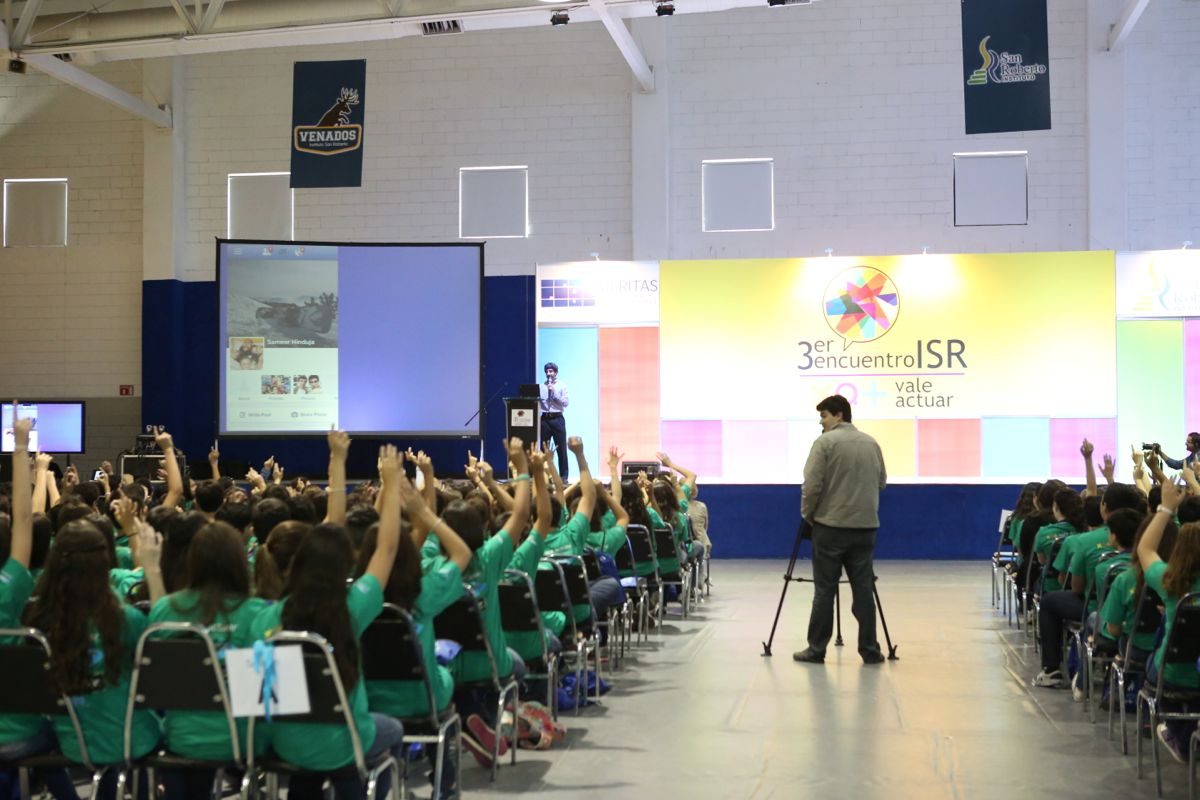 Sameer Hinduja presenting to a full hall of students with hands raised during an interactive assembly